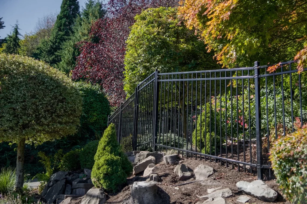Black metal ornamental fence expertly installed along a challenging, rocky slope in a heavily landscaped, residential setting.