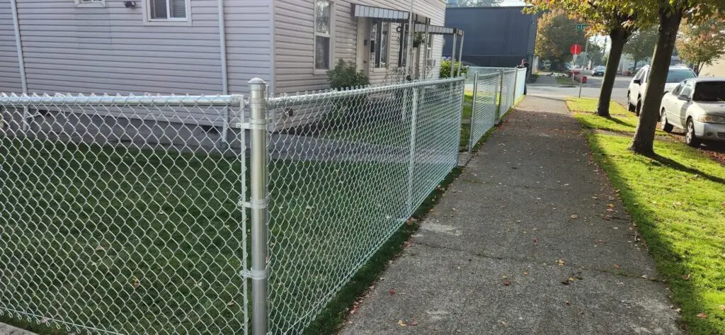Another angle of a chain link fence installed around a property, with a sidewalk visible in the foreground.