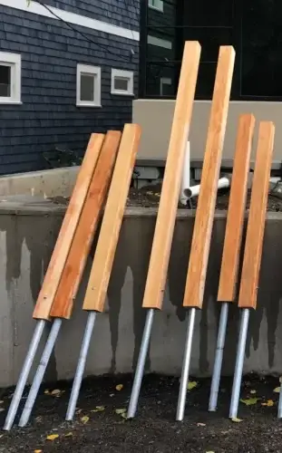 A set of wooden fence posts with steel pipes ready for installation using post-on-pipe technology. The posts are placed next to a concrete foundation, ready for a secure and long-lasting fence.