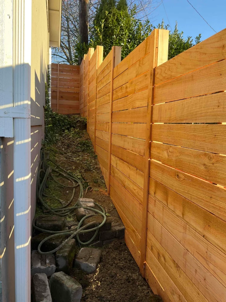 A high horizontal cedar fence running alongside a house on a steep, narrow slope, built to comply with Horizontal fence height rules.