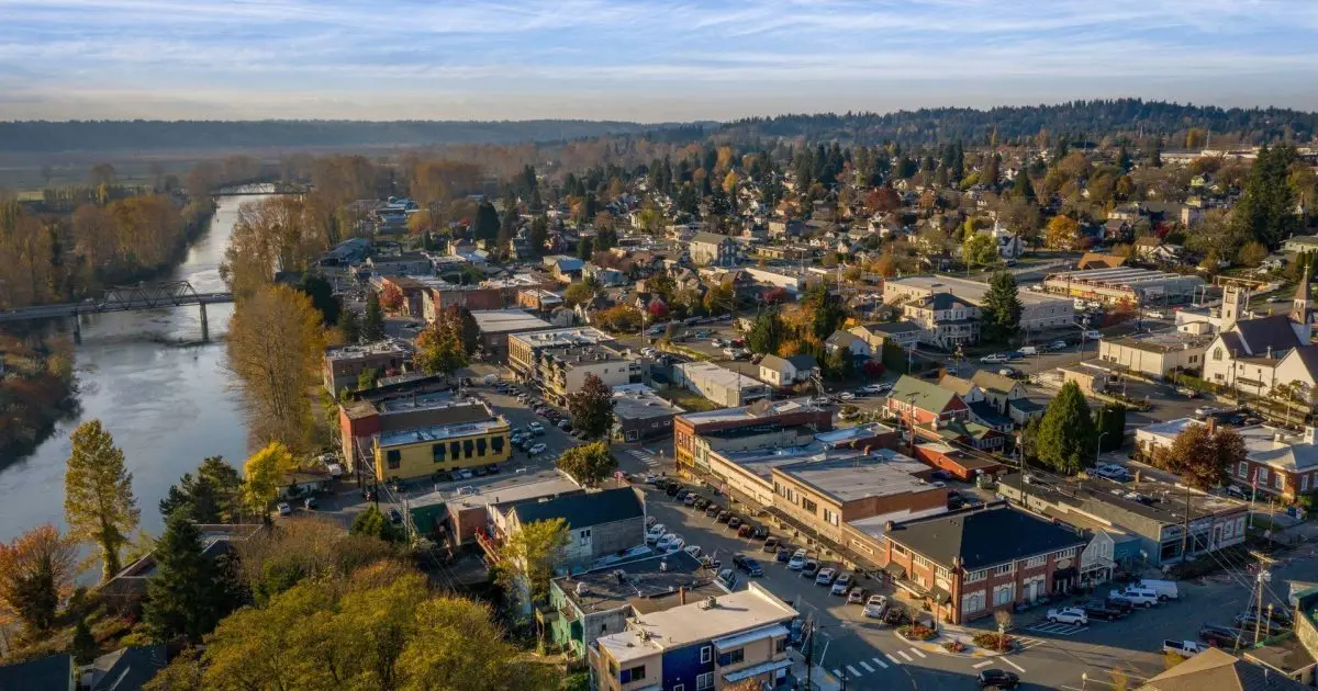 Aerial view of downtown Snohomish, WA, with a river, bridges, and a mix of historic buildings and homes, surrounded by autumn trees and distant hills.
