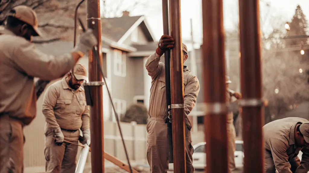 A professional team of fence installers working on-site. The image shows workers in uniform handling large metal posts and preparing for fence installation using post-on-pipe technology.