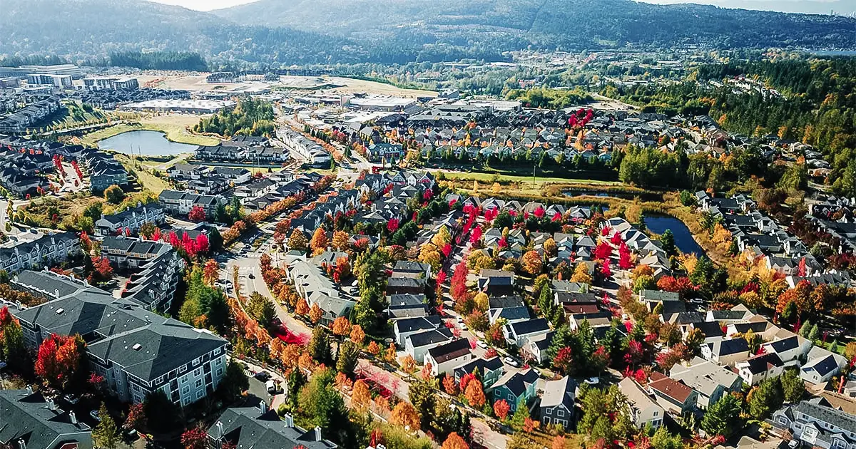 Aerial view of a suburban neighborhood with houses, autumn trees, and a small lake.