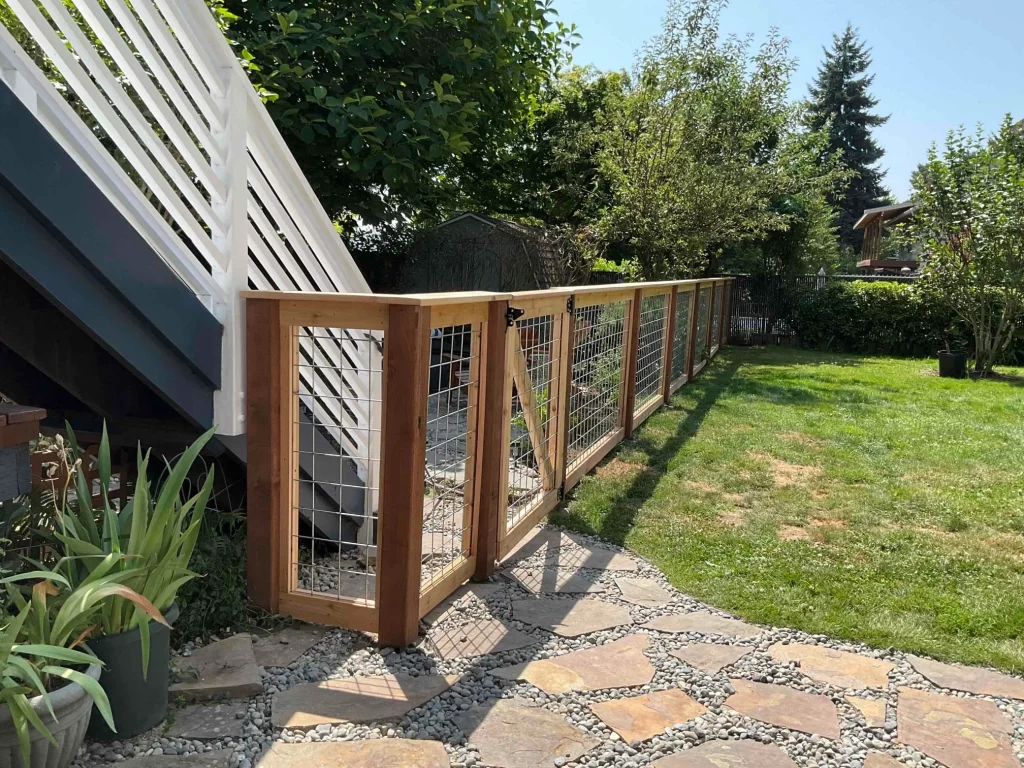 A backyard fence with hog wire deck railing and a wooden frame, leading to a lawn and garden.