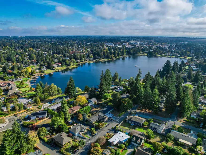 Aerial view of Burien, WA, with Lake Burien, homes, and dense trees under a blue sky.