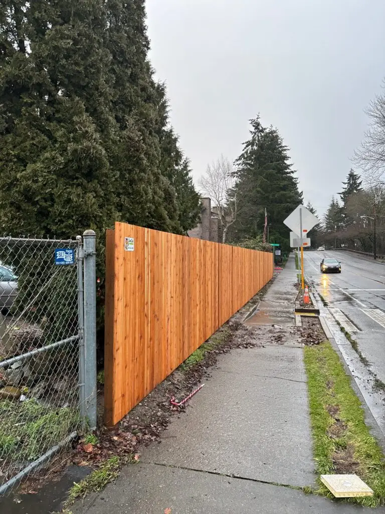 Cedar Estate Fence in Kent installed near a wet sidewalk with scattered debris and a traffic cone, during a rainy day