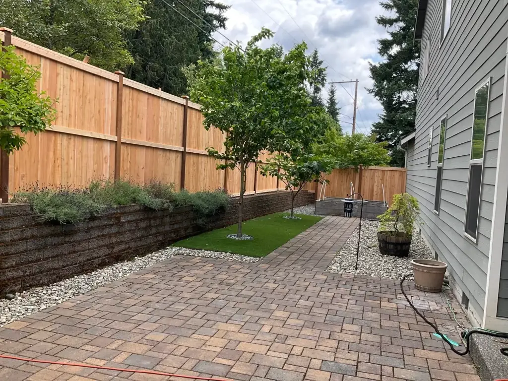 A cedar fence surrounds a landscaped yard with pavers and plants, perfect for Cedar Fences Seattle installations.