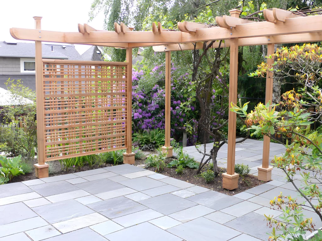 A wooden pergola over a stone patio, featuring a built-in lattice screen for privacy, emphasizing versatile pergola walls.