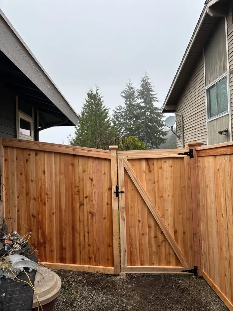 Full Panel Cedar Fence with Decorative Lattice Installed in Renton in a backyard with garden beds and a large tree, on a cloudy day.