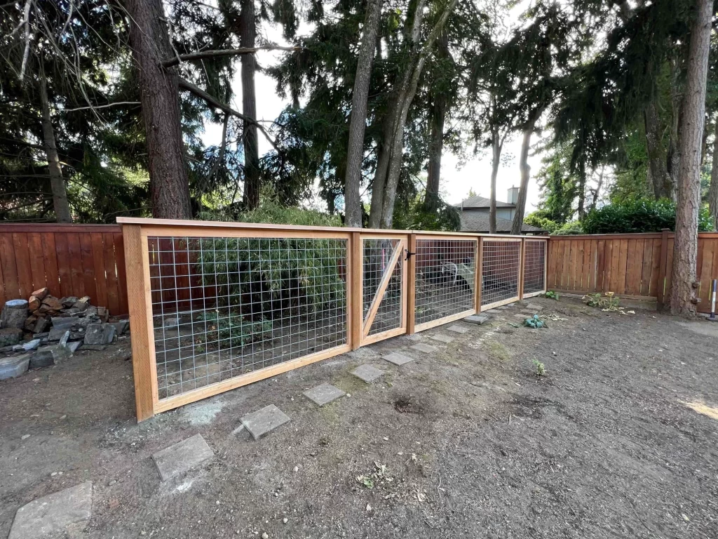 A backyard hog wire fence with wooden framing and a gate, showing the materials and design, helping to understand hog wire fence cost.