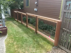 A newly installed hog wire fence with wooden framing along a side yard, demonstrating materials and structure, related to hog wire fence cost.