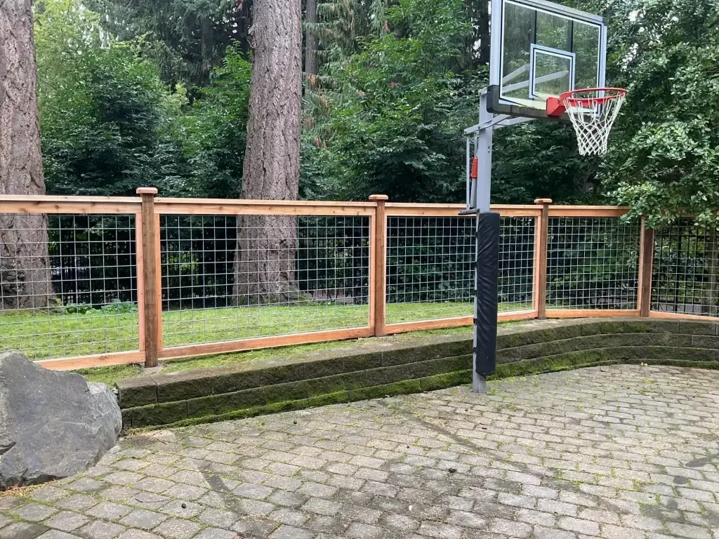 A sturdy wooden fence with hog wire panels, protecting a backyard basketball court while blending with nature.