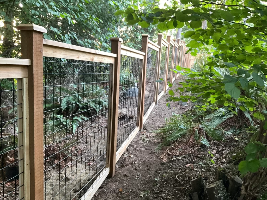 A hog wire fence with wooden posts, offering security and visibility while blending with a natural, wooded setting.