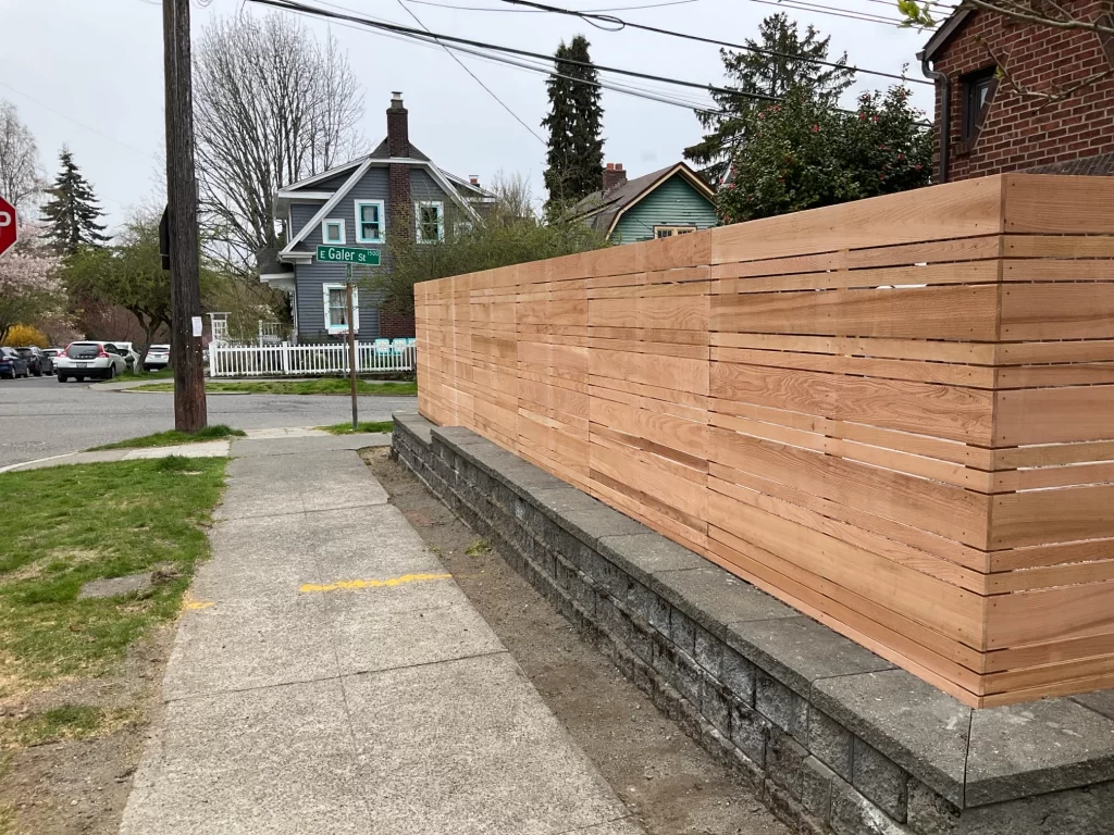 A horizontal cedar fence extends along the sidewalk, showcasing its sleek, contemporary style. For those considering this project, the horizontal cedar fence installation cost in Seattle may vary based on the scope.