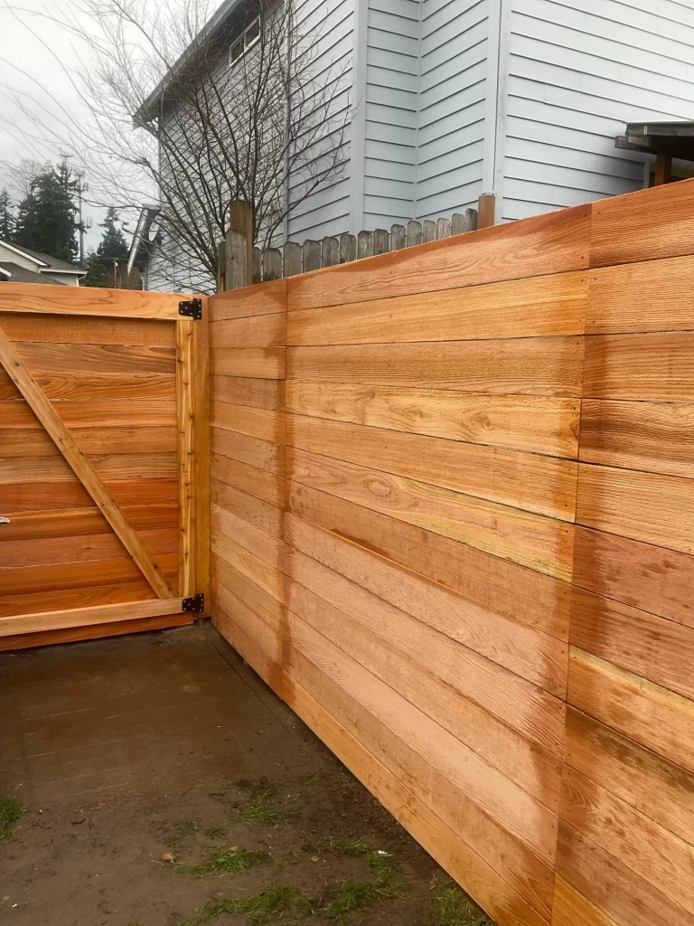 Newly installed horizontal cedar fence showcasing its clean design, with the gate in the foreground. For an accurate estimation, consider the horizontal cedar fence installation cost in Seattle.