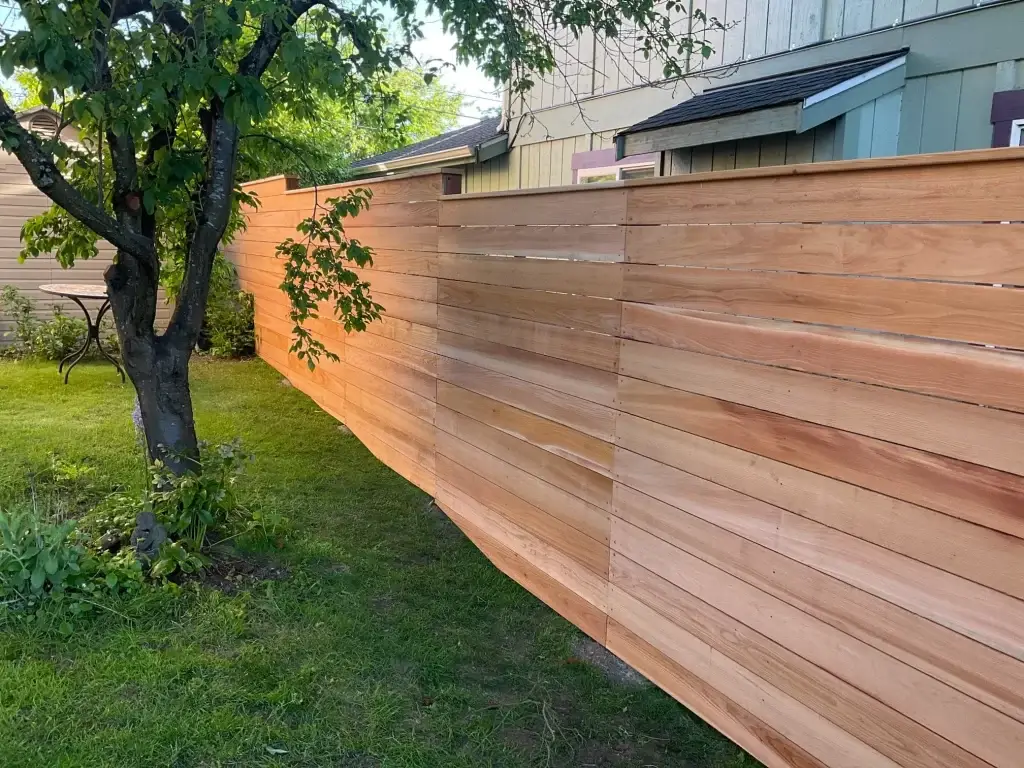 A horizontal cedar fence running along a yard, with smooth lines and a natural finish, blending with the surrounding landscape.