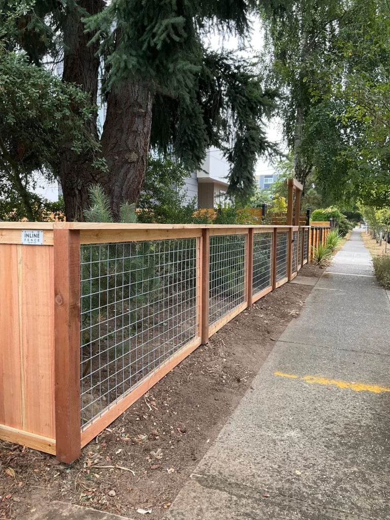 A side view of a wooden fence with hog wire deck railing, installed by Inline Fence, along a sidewalk.