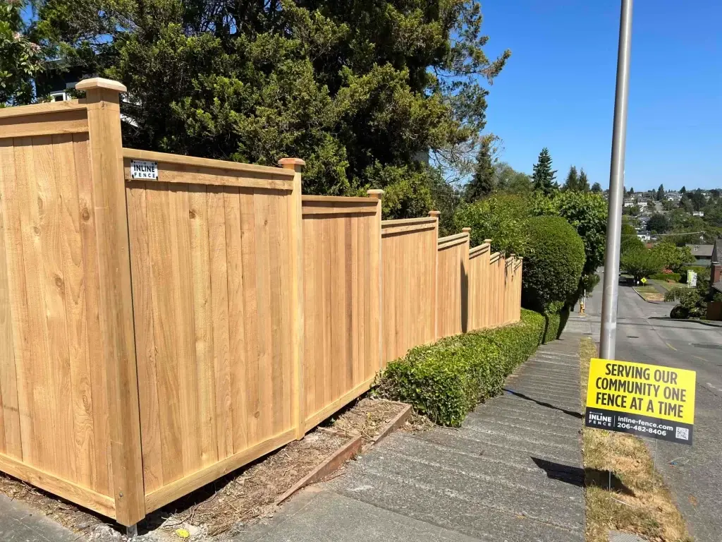 A cedar fence lining a street with a sign promoting Inline Fence. Cedar fence maintenance Seattle ensures long-term durability and beauty.