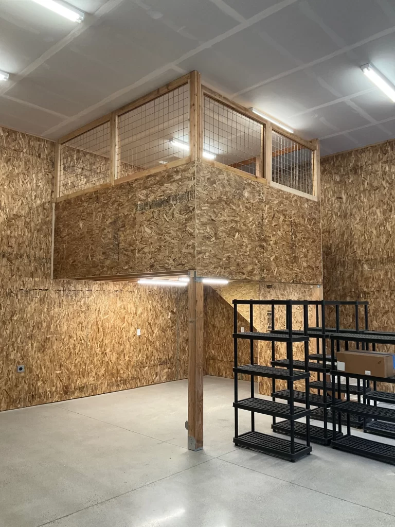 A mezzanine with wooden walls and a hog wire railing in a spacious industrial room.