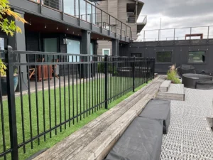 A black ornamental iron fence around a deck area with artificial grass and outdoor seating.