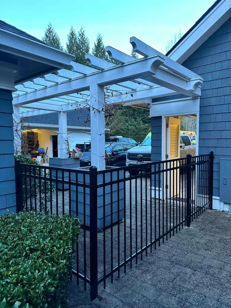 A black ornamental iron fence around a pergola in front of a house.