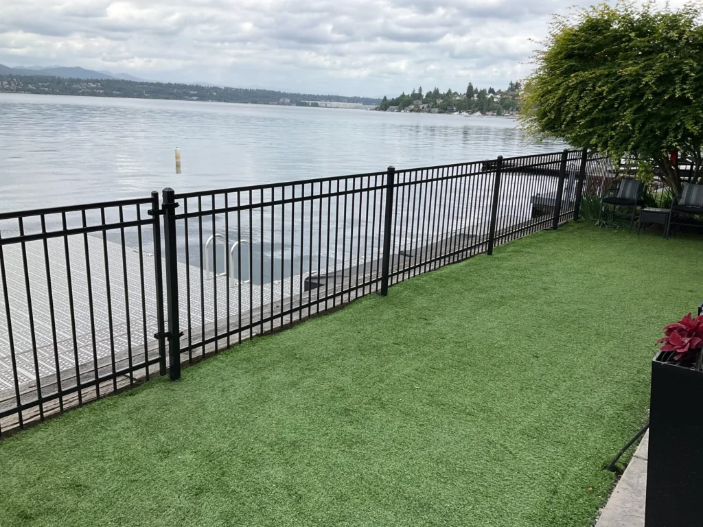A black ornamental iron fence along a lush green lawn, next to the water.