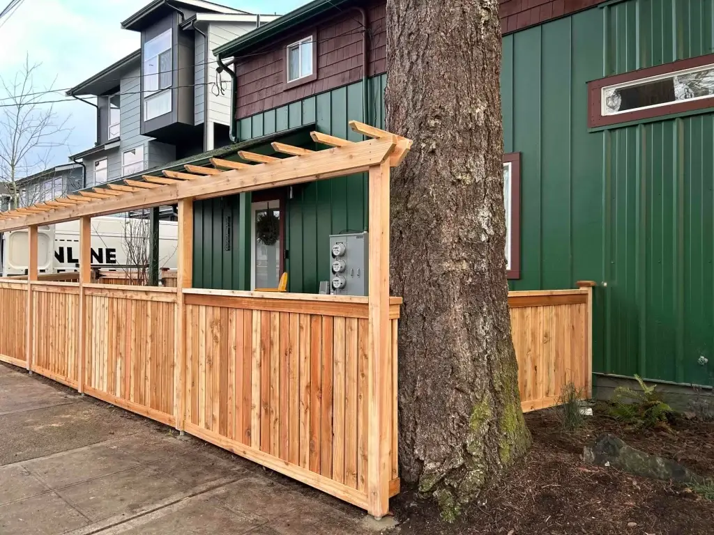 A pipe fence with wood panels and a pergola, wrapping around a tree for a unique residential design.