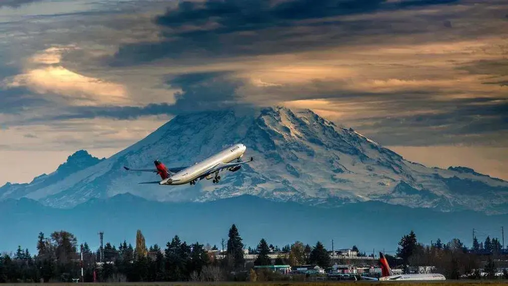 Plane at SeaTac, WA, with Mount Rainier and cloudy sky in the background.