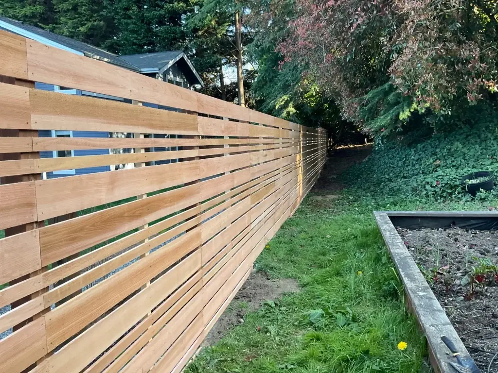 A sleek wooden fence with horizontal slats, ideal for Summer Fence Installation in Seattle's natural surroundings.