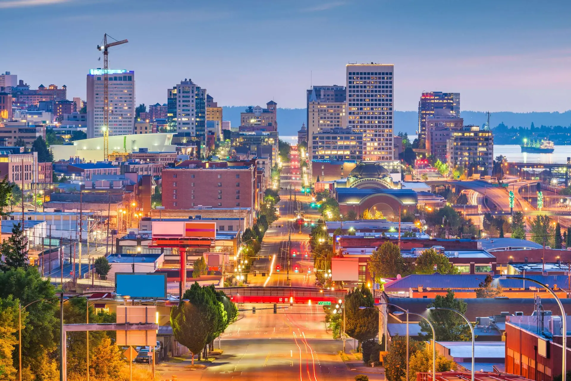 Tacoma, WA skyline at dusk with lit-up buildings, streets, and a waterfront view.