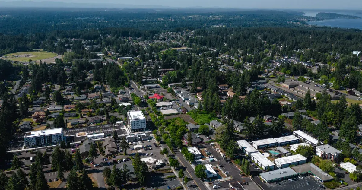 Aerial view of University Place WA showcasing lush forests, residential neighborhoods, modern buildings, and a scenic bay in the distance.