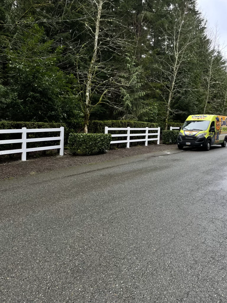 A white vinyl fence installed along a roadway with evergreen trees, illustrating the vinyl fence cost in Seattle.