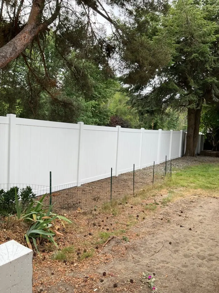 A white vinyl privacy fence installation Normandy Park, providing privacy and durability next to trees and landscaping.