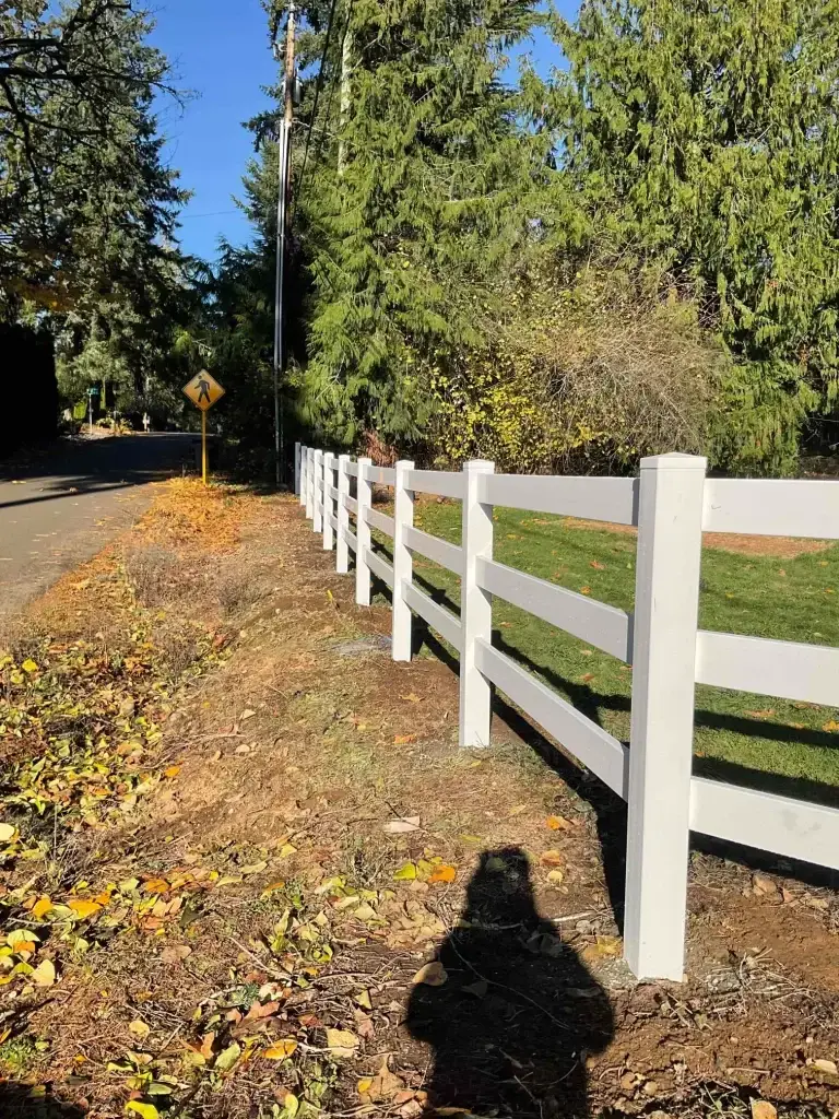 A white vinyl post and rail fence surrounded by greenery, offering inspiration for vinyl fence decorating ideas.