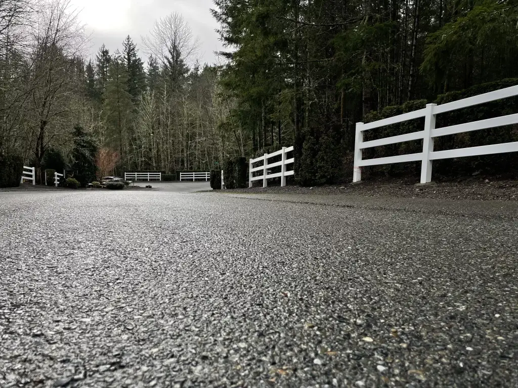 A white vinyl post and rail fence lines a paved road, creating a clean and neat appearance, showcasing vinyl fence decorating ideas.